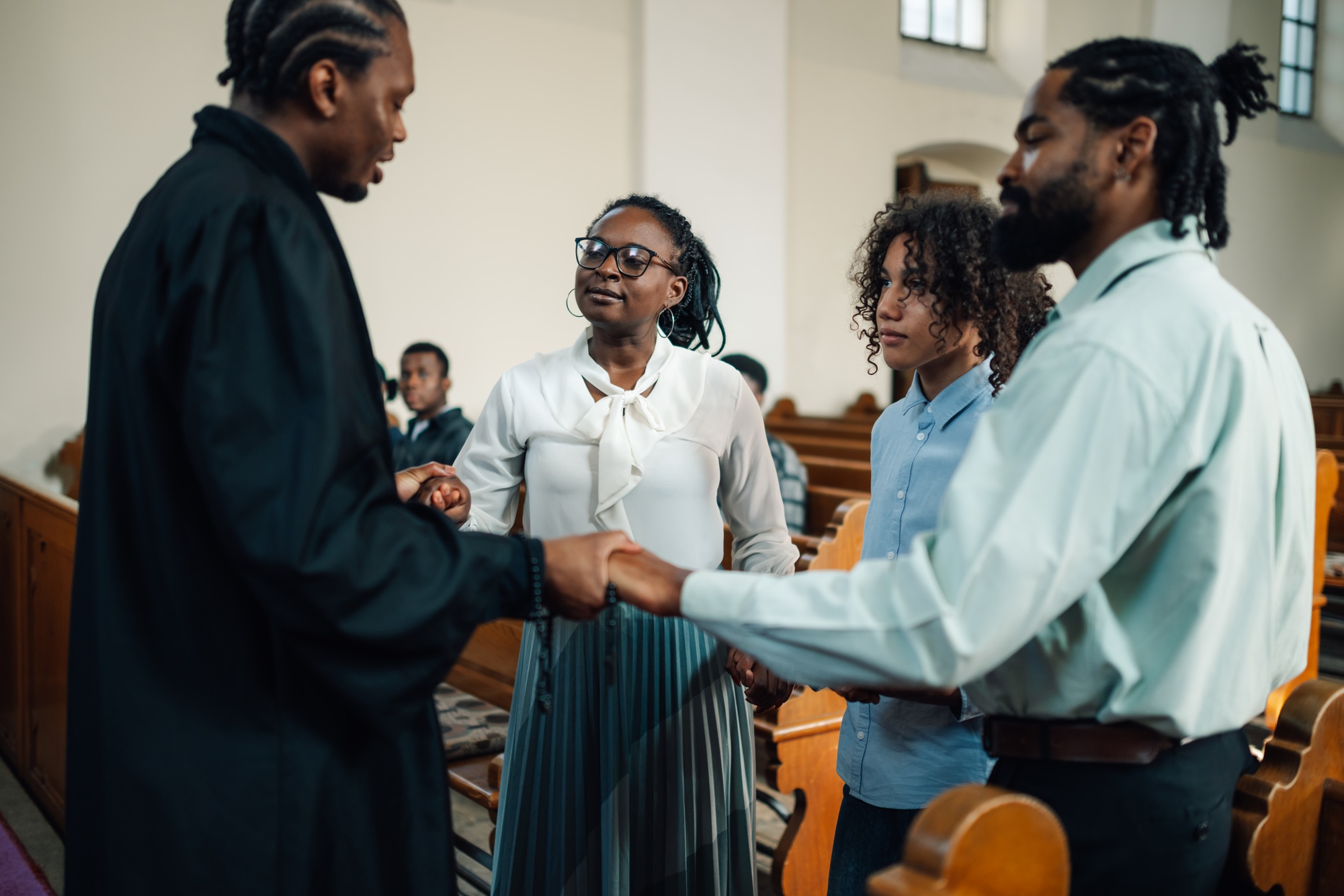 Priest holding hands with family praying in church